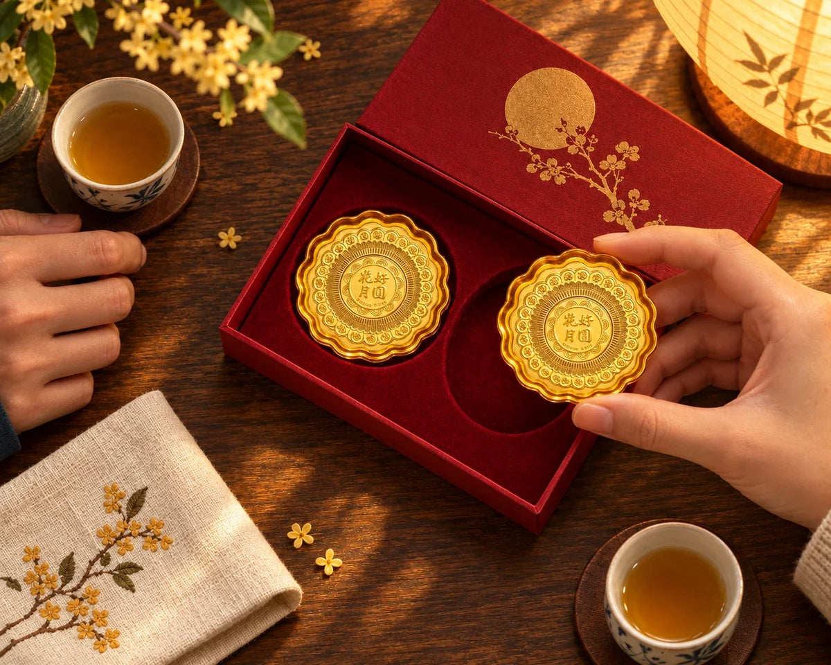 Gold mooncake keepsakes in an open presentation box beside tea cups.